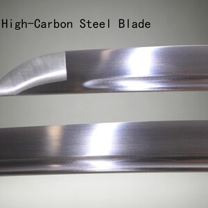 May include: A high-carbon steel blade with a polished, reflective metallic surface. The blade features a curved tip and a distinct edge line. The text "High-Carbon Steel Blade" is printed in black above the upper section of the metal blade.