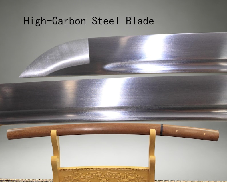 May include: A high-carbon steel blade with a polished metallic finish and a curved edge, positioned above a smooth, light brown wooden scabbard resting on a light-colored wooden stand. The text High-Carbon Steel Blade is visible above.