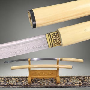 May include: A Japanese-style sword with a curved, patterned steel blade and a light-colored wooden handle and scabbard. The sword features a gold-toned metal collar with an intricate cutout design, displayed on a wooden stand with carved details.