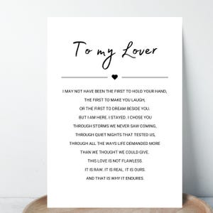 Puede incluir: Una impresión blanca con el texto "To my Lover" en una fuente manuscrita, con un símbolo de corazón negro. El texto de abajo dice: "Puede que no haya sido el primero en tomar tu mano... Este amor no es perfecto. Es crudo. Es real. Es nuestro. Y por eso perdura."