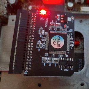 May include: A black circuit board with a red LED light and a "QC PASSED" sticker is connected to a larger green circuit board. The image shows electronic components, including chips and connectors, with a focus on the black board.