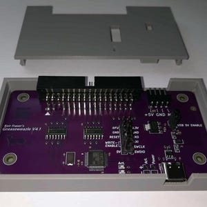 Könnte beinhalten: Eine lila Leiterplatte mit der Aufschrift "Keir Fraser's Greaseweazle V4.1" mit verschiedenen elektronischen Bauteilen, Stiften und einem USB-Anschluss. Die Platine befindet sich in einem grauen Kunststoffgehäuse mit passendem Deckel.