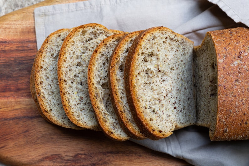 May include: Close-up of sliced bread with a grainy texture. The bread is light brown and has a slightly crispy crust.