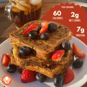 May include: A plate of French toast topped with fresh strawberries and blueberries. The toast is golden brown and has a crispy exterior. The plate is white and has a light brown wooden background. The text *Per Serving* is visible in the upper right corner of the image. The text *60 Calories* is visible in the upper right corner of the image. The text *2g Net Carbs* is visible in the upper right corner of the image. The text *7g Protein* is visible in the upper right corner of the image.