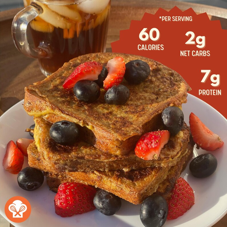 May include: A plate of French toast topped with fresh strawberries and blueberries. The toast is golden brown and has a crispy exterior. The plate is white and has a light brown wooden background. The text *Per Serving* is visible in the upper right corner of the image. The text *60 Calories* is visible in the upper right corner of the image. The text *2g Net Carbs* is visible in the upper right corner of the image. The text *7g Protein* is visible in the upper right corner of the image.