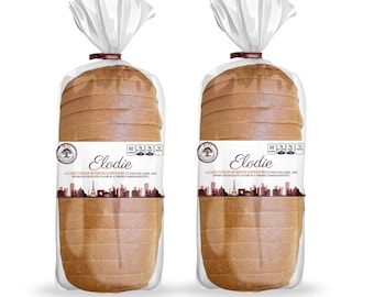 May include: Two loaves of sliced bread in clear plastic packaging. Each loaf has a label that reads "Elodie" with a cityscape design. The bread is light brown and appears to be a sandwich loaf.