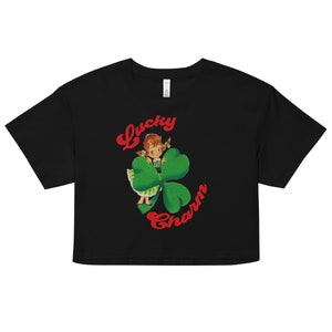 May include: Black cropped t-shirt with a red and green graphic of a girl standing behind a four-leaf clover. The text "Lucky Charm" is written in red cursive.
