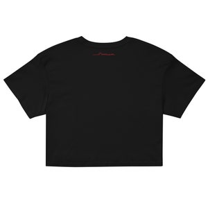 May include: Black cropped t-shirt with short sleeves. The shirt has a small red logo on the back.