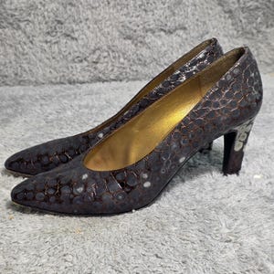 Peut inclure: Une paire d'escarpins marron foncé avec un motif texturé en forme de reptile. Les chaussures ont des bouts pointus, un intérieur doré et un talon d'environ 7.6 cm de hauteur.