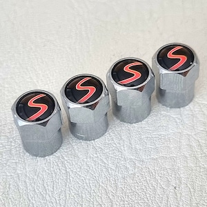 Pode incluir: Conjunto de quatro tampas de válvula de pneu prateadas com um logotipo "S" vermelho e preto.