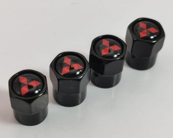 Puede incluir: Juego de cuatro tapones de válvula de neumático negros con un logotipo de Mitsubishi rojo.