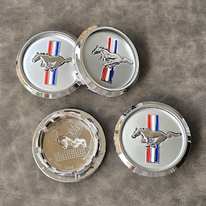 May include: Four silver car hubcaps with a red, white, and blue running horse logo. The hubcaps are chrome and have a raised edge.