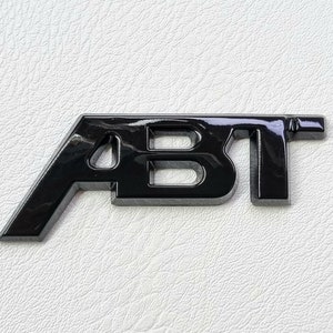 以下が含まれることがあります： スタイリッシュなフォントで「ABT」と書かれた、黒光りするプラスチック製のエンブレムです。