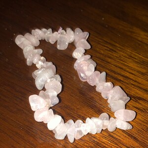 May include: A pink rose quartz chip bracelet with a delicate, natural look. The bracelet is made of small, irregular shaped stones that are strung together on a clear elastic cord.