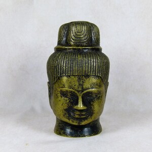 Peut inclure: Une sculpture en bronze d'une tête de Bouddha avec une coiffure détaillée. La sculpture est de couleur vert foncé et a une expression sereine.