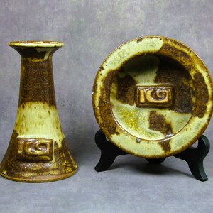 May include: A set of two ceramic pieces in a brown and green glaze. The larger piece is a shallow dish with a raised design in the center. The smaller piece is a vase with a similar design. Both pieces have a brown and green glaze with a white swirl design.