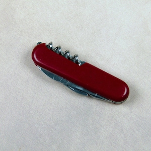 May include: A red pocket knife with a silver blade and a corkscrew.