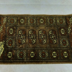 May include: A brown rug with a geometric pattern in shades of brown, beige, and cream. The rug has a fringe border on all sides.
