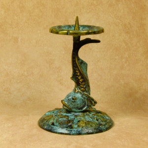 May include: A teal and gold metal candle holder shaped like a fish. The holder has a round top with a spike for a candle.