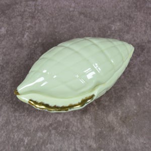 Peut inclure: Un plat en céramique en forme d'épi de maïs vert pâle avec un motif matelassé. Les bords sont dorés. L'objet est décoratif, probablement pour servir ou exposer.