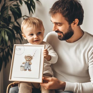 May include: A framed watercolor illustration of a brown bear wearing a blue fishing hat and overalls, holding a fishing rod and a bucket of fish. The bear is standing on a white background. The frame is made of light wood.