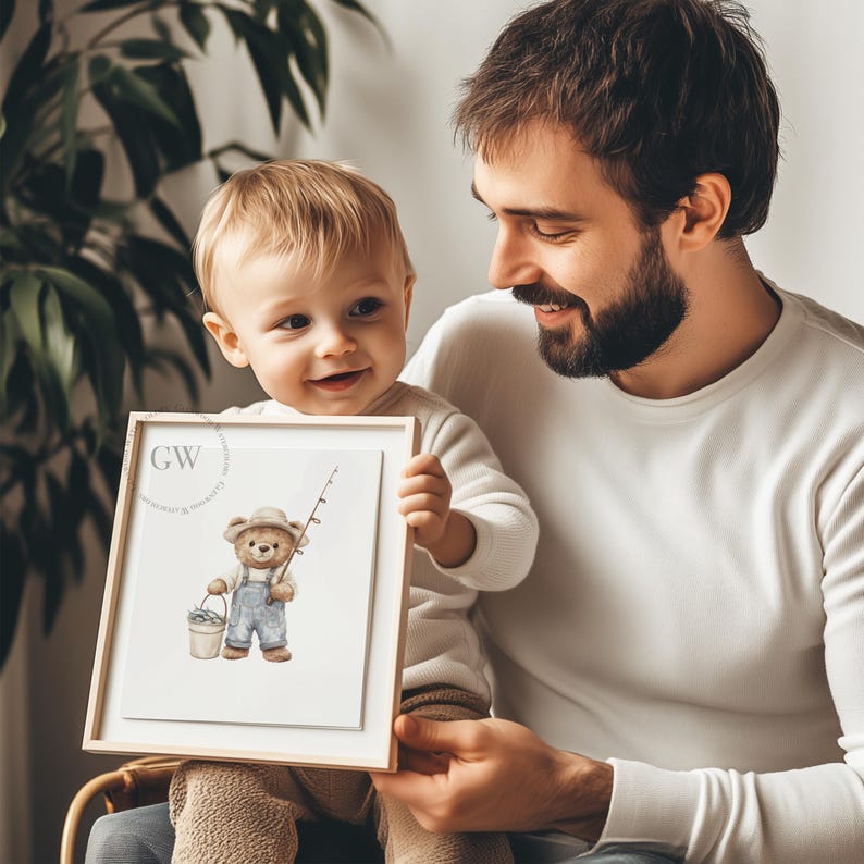 May include: A framed watercolor illustration of a brown bear wearing a blue fishing hat and overalls, holding a fishing rod and a bucket of fish. The bear is standing on a white background. The frame is made of light wood.