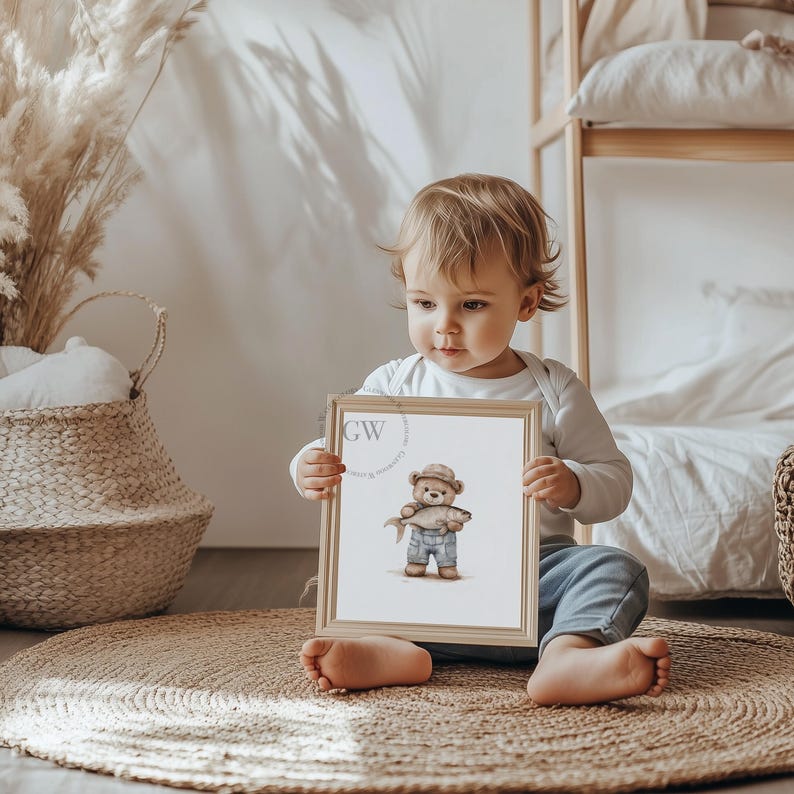 May include: A child holds a framed print of a brown teddy bear wearing a blue shirt and a hat, holding a fish. The print has a white background and a wooden frame.