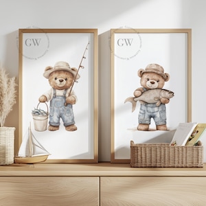 May include: Two framed prints of watercolor illustrations of teddy bears fishing. The bear on the left is holding a fishing rod and a bucket of fish. The bear on the right is holding a fish. Both bears are wearing overalls and hats. The prints are on a wooden shelf.