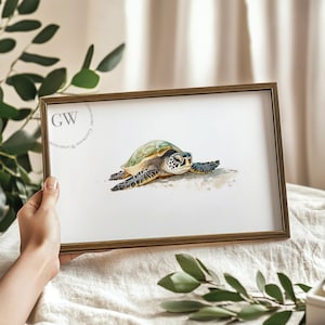 Puede incluir: Una pintura de acuarela enmarcada de una tortuga marina verde con caparazón marrón descansando en una playa de arena. La tortuga tiene los ojos cerrados y la cabeza inclinada hacia un lado. La pintura está en un marco dorado.