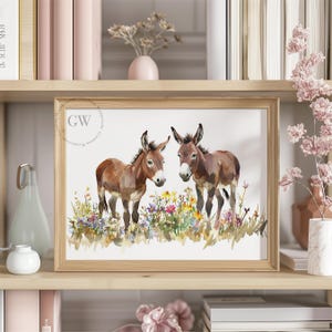 Puede incluir: Una pintura de acuarela de dos burros marrones de pie en un campo de flores silvestres. Los burros miran al espectador y tienen una expresión amigable. El fondo es un suave lavado de acuarela azul y verde.