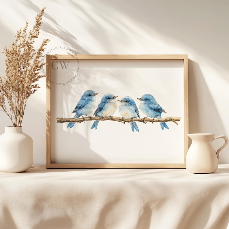 May include: A watercolour painting of four bluebirds perched on a branch. The birds are facing to the right and have light blue bodies with darker blue wings and tails. The painting is framed in a light wood frame.