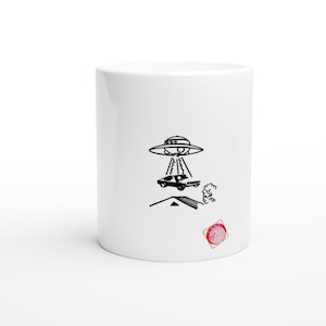 May include: A white ceramic mug featuring a black line drawing of a flying saucer abducting a car from the roof of a house. A small red square stamp with a spiral design is located in the lower right corner of the mug's exterior surface.