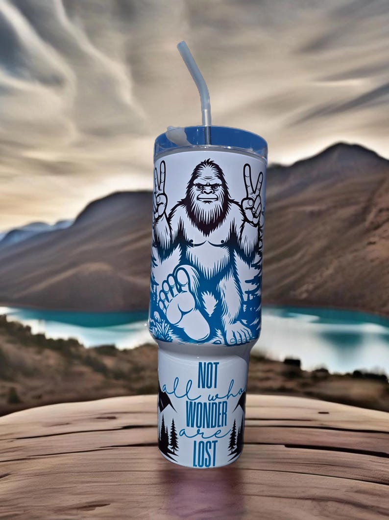 May include: White tumbler with a blue and black graphic of a Bigfoot with the text "Not all who wander are lost".