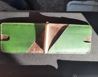 May include: A green and brown leather wallet with a metal money clip. The wallet has a stitched edge and is folded in half.