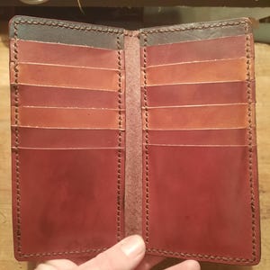 May include: Open leather wallet with multiple card slots. The wallet is open, revealing a gradient of colors from dark brown to red. The edges are stitched with a contrasting thread.