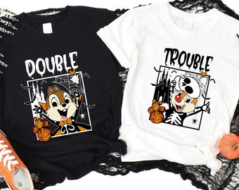 Puede incluir: Dos camisetas con temática de Halloween, una negra y otra blanca. La camiseta negra dice "DOUBLE" con una ardilla de dibujos animados sosteniendo calabazas. La camiseta blanca dice "TROUBLE" con un personaje de dibujos animados con disfraz de esqueleto. Ambas camisetas tienen gráficos de Halloween.