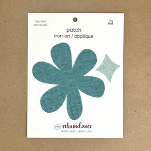 May include: A teal blue flower-shaped iron-on patch with a smaller teal blue diamond-shaped patch. The patches are made from upcycled materials and are labeled "patch iron-on/applique" and "rebundance create more + waste less".