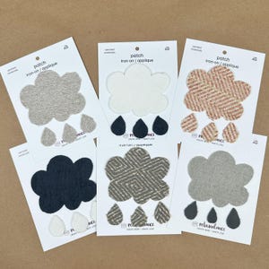 May include: Five iron-on patches featuring a cloud and raindrops in various colors and textures. The patches are packaged on white cards with the text "patch iron-on/applique" and "rebundance create more waste less".