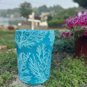 Peut inclure: Un panier de rangement cylindrique en tissu présentant un fond turquoise vif avec un motif répétitif de corail blanc. Le contenant a une forme droite et structurée, fabriqué dans une matière textile souple avec un bord supérieur fini.
