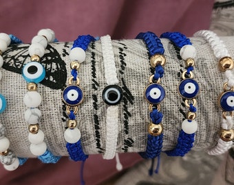 May include: A set of seven bracelets with blue evil eye charms. The bracelets are made with white beads, blue string, and gold beads.