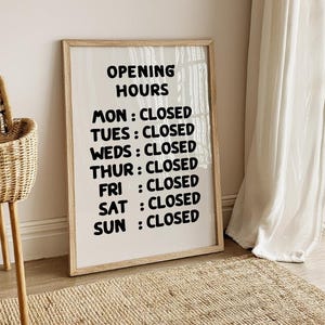 May include: A white framed sign with black text that reads "Opening Hours" and lists the days of the week with the word "Closed" next to each day.