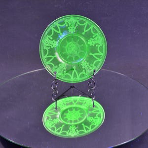 May include: A green glass plate with a decorative design of a ship's wheel and other nautical motifs. The plate is on a black stand and reflected in a mirror.