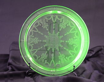May include: A green glass plate with a decorative etched design. The plate is on a black stand.