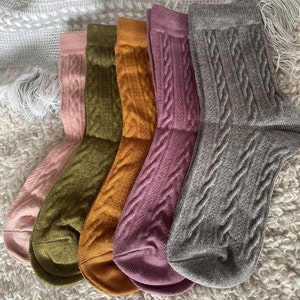 May include: Five pairs of cable knit socks in different colours: pink, green, orange, purple, and grey.