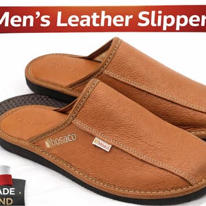 May include: A pair of brown leather slippers with a stitched design and a black sole. The slippers have a textured appearance and the text "Men's Leather Slippers" is displayed on a red banner. The slippers are handmade in Poland.