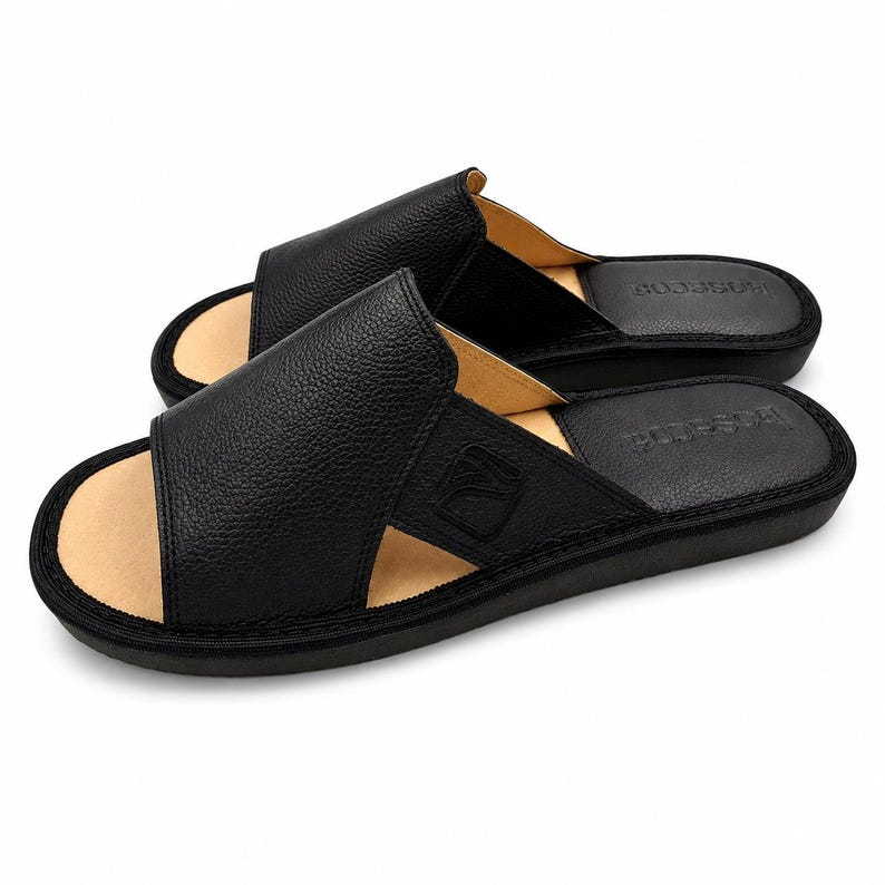 May include: A pair of black leather slide sandals with a textured pebble grain finish on the wide upper strap. The sandals feature a tan interior lining, a black footbed with the embossed text "basarim", and a black sole with stitched edges.