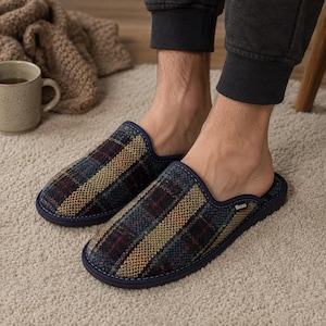 May include: A pair of plaid pattern slippers with a navy blue trim. The slippers have a dark color scheme with red, yellow, and blue accents. The slippers are on a light-colored carpet.
