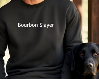 May include: Black sweatshirt with the text "Bourbon Slayer" in white. A black Labrador Retriever dog is next to the sweatshirt. The sweatshirt is part of a matching black sweatsuit.