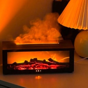 Może przedstawiać: Prostokątny, ciemnobrązowy kominek elektryczny z jasno pomarańczowym i czerwonym wnętrzem, emitujący obłok pary. Kominek stoi na białej powierzchni, z lampą i czarnym przedmiotem w tle.