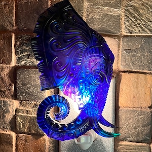 May include: A blue glass night light shaped like an elephant with intricate details. The light is illuminated and casts a warm glow.